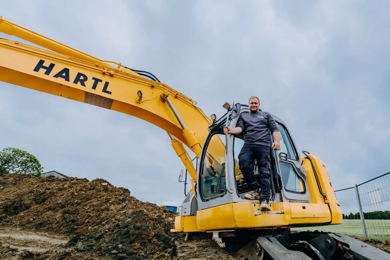 Gelber Hartl-Bagger mit Mitarbeiter auf der Kabine
